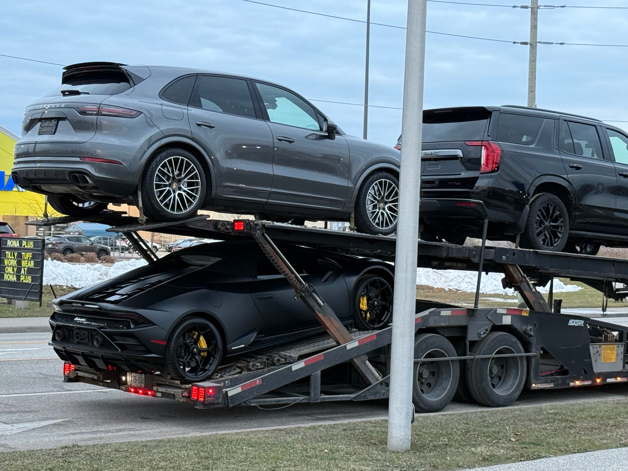 Double-deck car carrier loaded with a Porsche Cayenne and a matte black Lamborghini Huracan